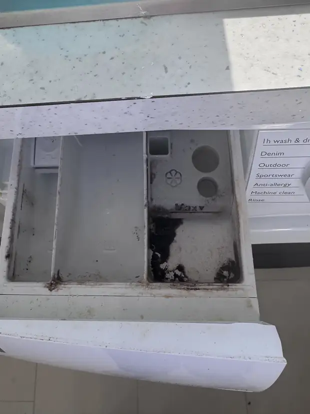 Washing machine detergent drawer with heavy black mould and detergent build-up before cleaning